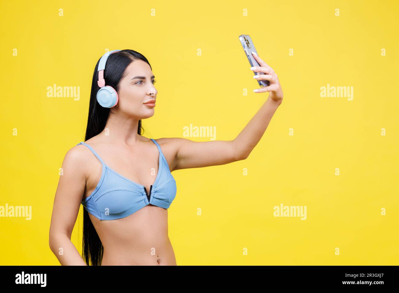 Porträt eines jungen, hübschen Mädchens mit kabellosen Kopfhörern auf dem Kopf, Selfie für soziale Netzwerke, lächelnd und lachend an der Telefonkamera, isoliert auf y Stockfoto