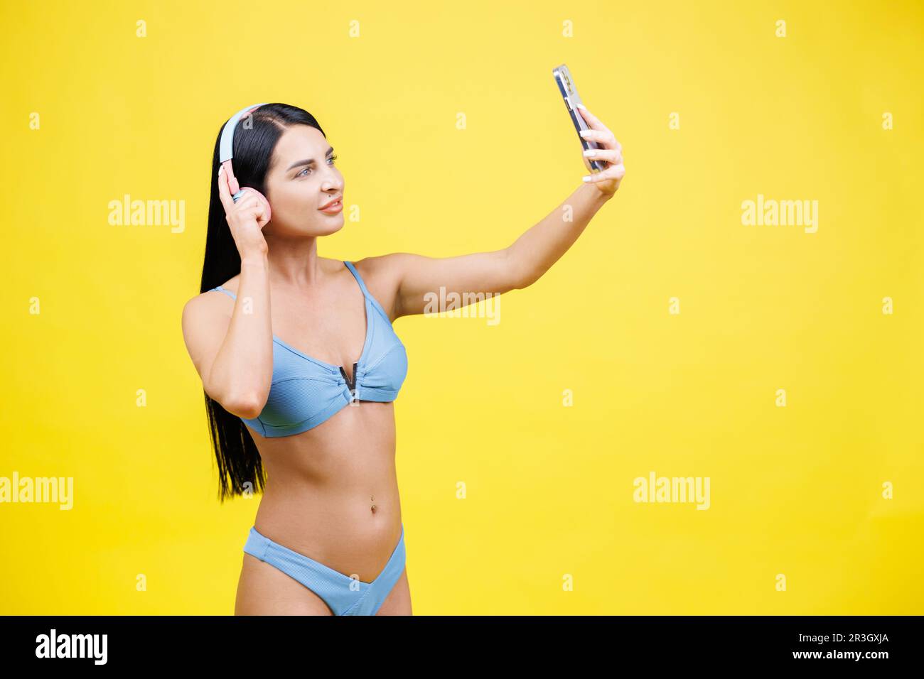 Porträt eines jungen, hübschen Mädchens mit kabellosen Kopfhörern auf dem Kopf, Selfie für soziale Netzwerke, lächelnd und lachend an der Telefonkamera, isoliert auf y Stockfoto