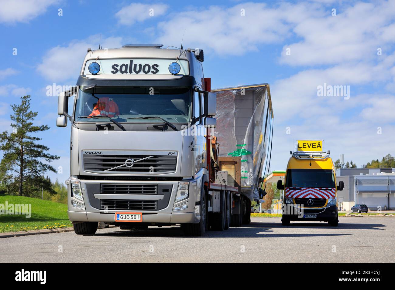 Volvo FH-Lkw, der eine Salvos-Blockkabine als außergewöhnliche Ladung transportiert, die auf einem LKW-Rastplatz mit einem Pilotfahrzeug geparkt ist. Forssa, Finnland. 19. Mai 2023. Stockfoto