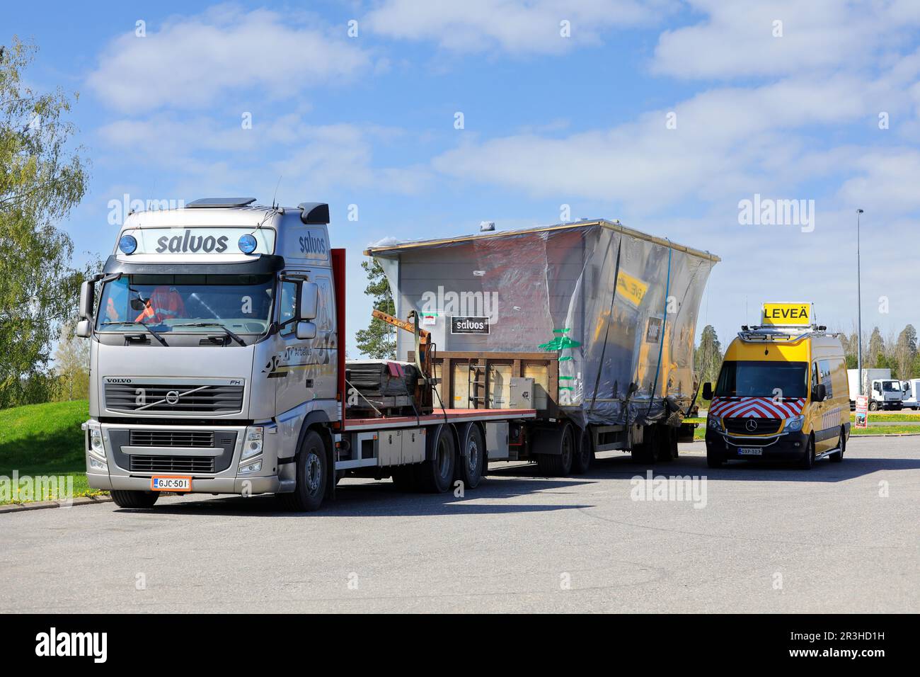 Volvo FH-Lkw, der eine Salvos-Blockkabine als außergewöhnliche Ladung transportiert, die auf einem LKW-Rastplatz mit einem Pilotfahrzeug geparkt ist. Forssa, Finnland. 19. Mai 2023. Stockfoto