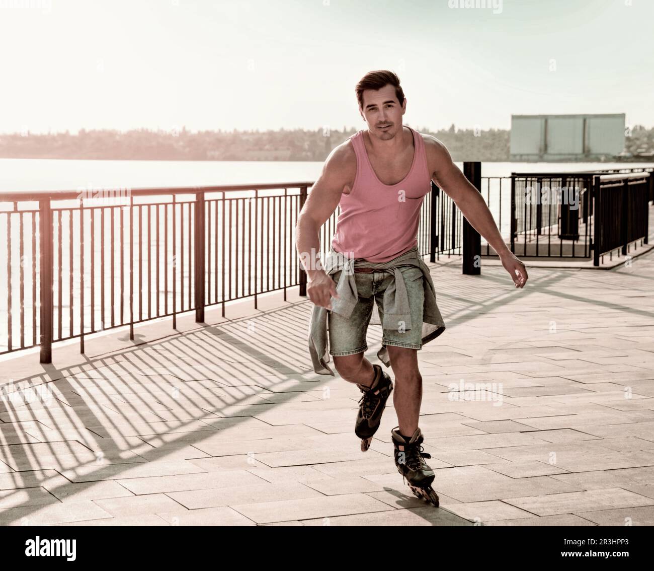 Attraktiver junger Mann, der Rollschuhlaufen auf dem Pier in der Nähe des Flusses macht, Platz für Text Stockfoto
