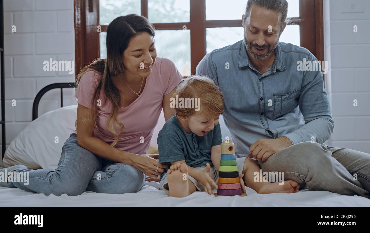 Glücklicher Sohn, der mit Mutter und Vater im Bett spielt, genießen Sie es, zusammen zu Hause zu entspannen. Stockfoto