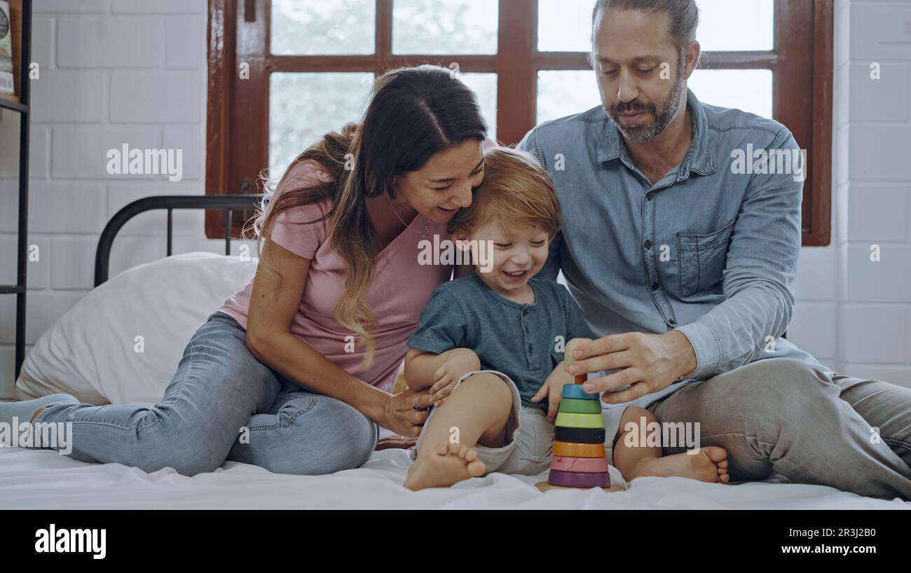 Glücklicher Sohn, der mit Mutter und Vater im Bett spielt, genießen Sie es, zusammen zu Hause zu entspannen. Stockfoto