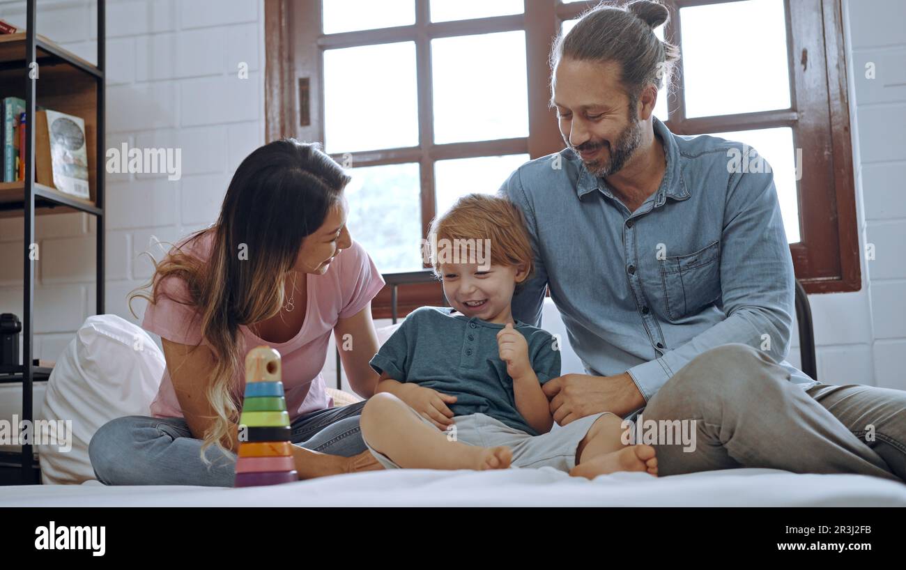 Glücklicher Sohn, der mit Mutter und Vater im Bett spielt, genießen Sie es, zusammen zu Hause zu entspannen. Stockfoto