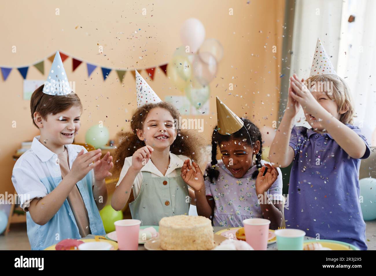 Vielfältige Gruppe von aufgeregten kleinen Kindern, die Konfetti werfen, während sie eine Geburtstagsparty für Kinder genießen und Spaß haben Stockfoto