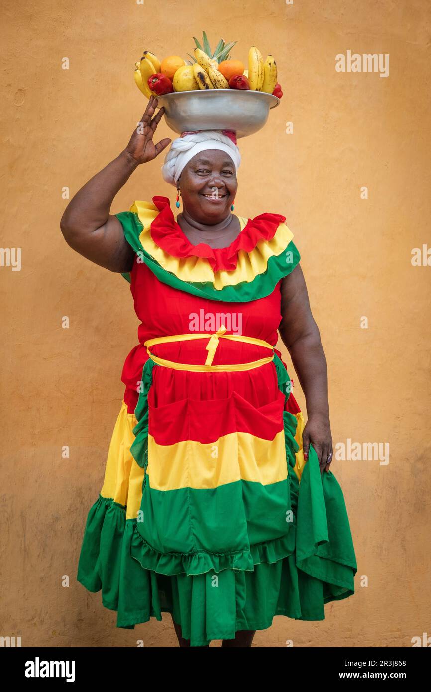 Fröhlicher Straßenverkäufer mit frischem Obst, auch bekannt als Palenquera, in der Altstadt von Cartagena, Kolumbien. Glückliche afrokolumbianische Frau in traditioneller Kleidung. Stockfoto