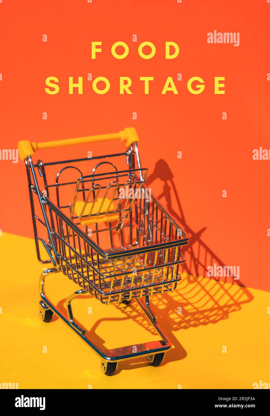 Text FÜR LEBENSMITTELKNAPPHEIT mit leerem Einkaufswagen auf isometrischem orangefarbenem gelben Hintergrund. Kleiner Spielzeugsupermarkt, Supermarkt, Supermarkt Stockfoto
