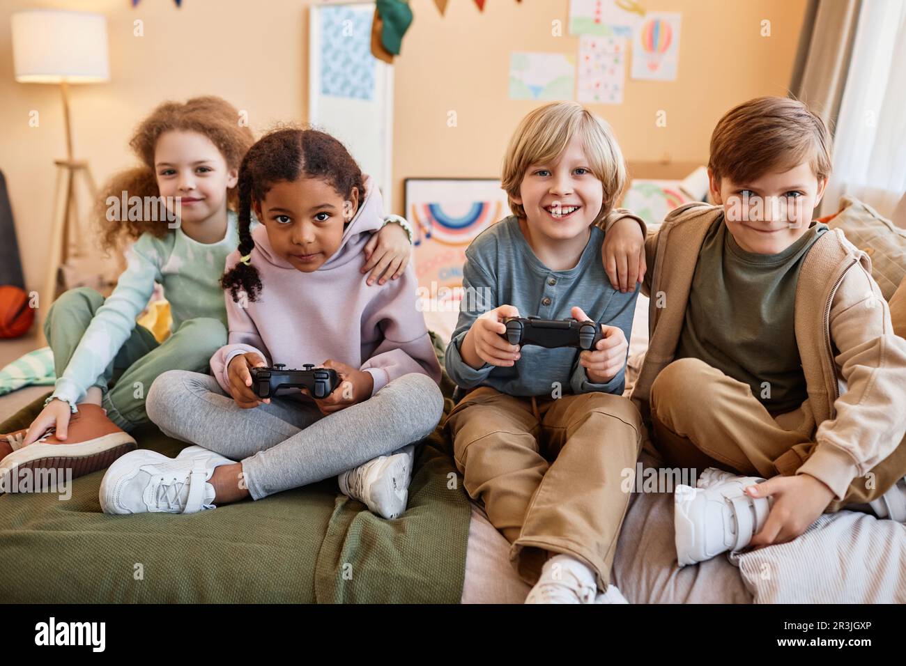 Vielfältige Gruppe glücklicher kleiner Kinder, die zusammen Videospiele spielen und Spaß haben Stockfoto