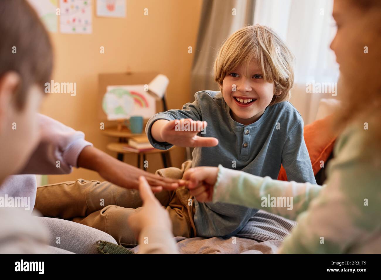 Gruppe von Kindern, die eine Steinpapierschere spielen, während sie im Kreis auf dem Bett sitzen, Kopierbereich Stockfoto