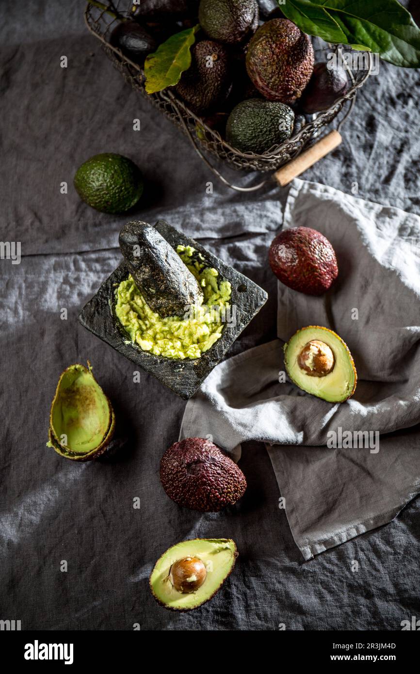 Avocado. Guacamole. Mexikanische Guacamole-Sauce in Steinmörtel, voller Korb mit Avocado, halbe Avocado auf Leinentischdecken. Oben Stockfoto