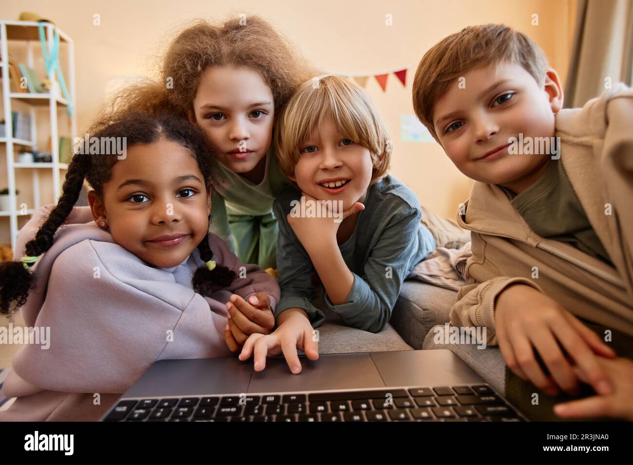 POV-Gruppe von Kindern, die zusammen auf einen Computerbildschirm schauen, sich über einen Laptop kuscheln und lächeln Stockfoto