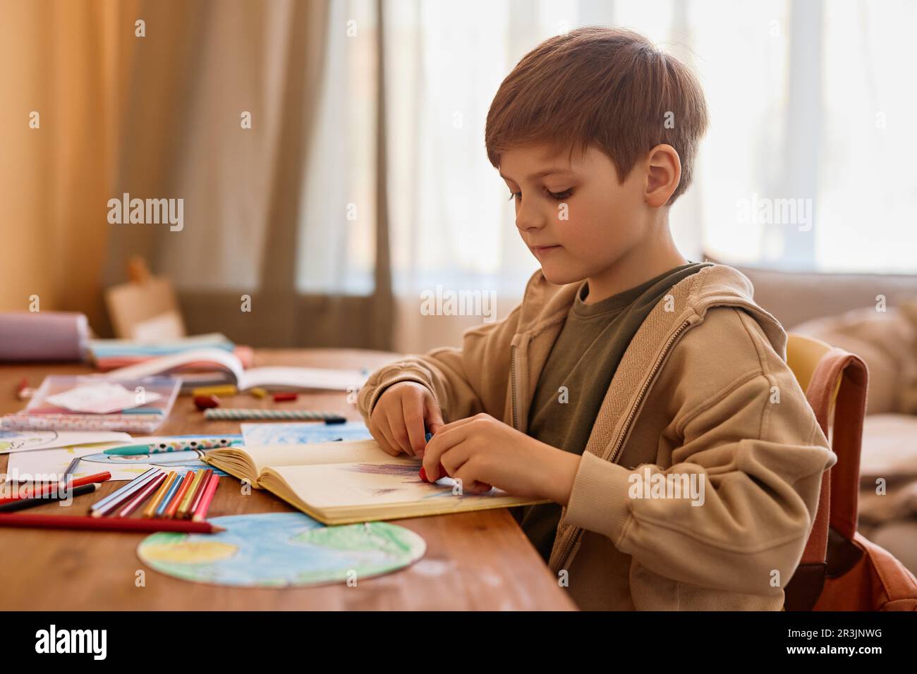Seitliches Porträt eines niedlichen Jungen, der an einem Tisch in einem gemütlichen Zimmer malt, Kopierbereich Stockfoto