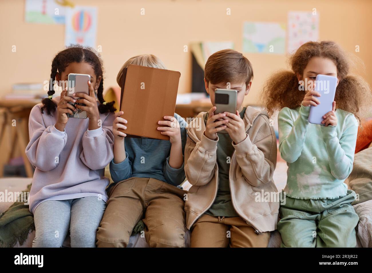 Gruppe kleiner Kinder, die Smartphones halten und Gesichter verstecken, Gen. Alpha Stockfoto