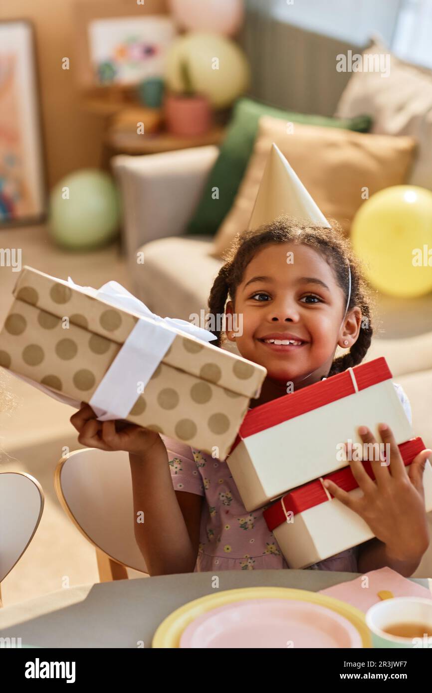Porträt eines kleinen schwarzen Mädchens, das Geschenke auf der Geburtstagsparty eröffnet und vor der Kamera lächelt Stockfoto