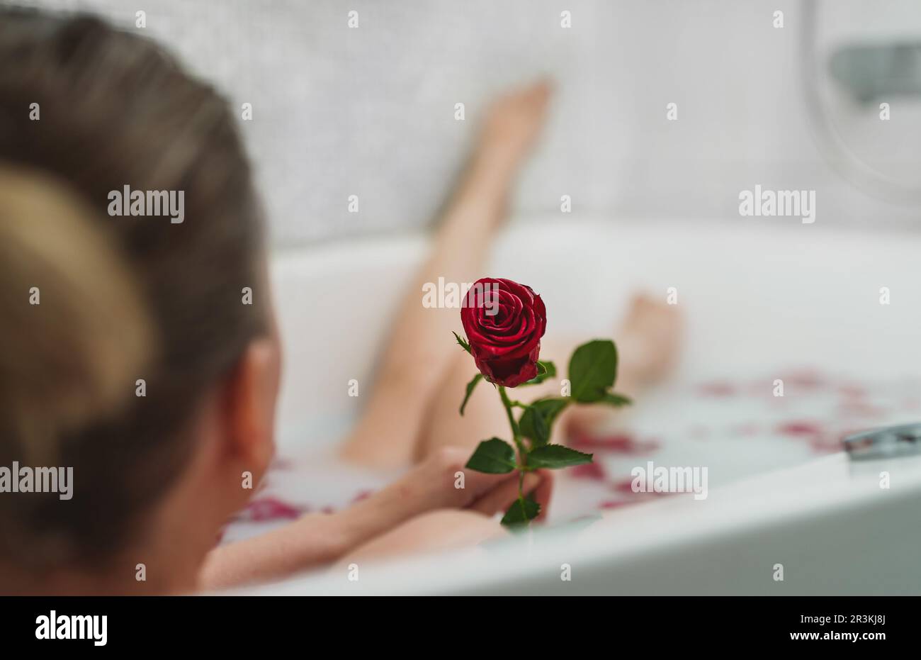 Die Frau entspannt sich in einem Bad mit Milch und Rosenblättern. Stockfoto