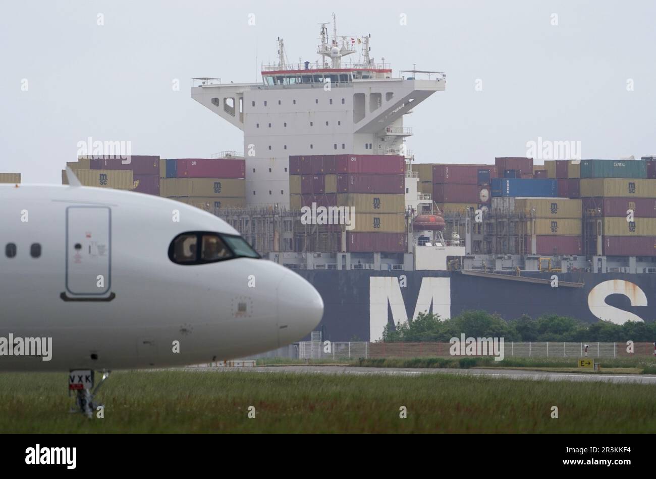 Hamburg, Deutschland. 24. Mai 2023. Ein Containerschiff der MSC-Schifffahrtsgesellschaft fährt auf der Elbe vorbei am Airbus-Werk in Finkenwerder. Die Fluggesellschaft Lufthansa hat den 600. Airbus, einen Airbus A321neo, in ihrer Flotte übernommen. Kredit: Marcus Brandt/dpa/Alamy Live News Stockfoto