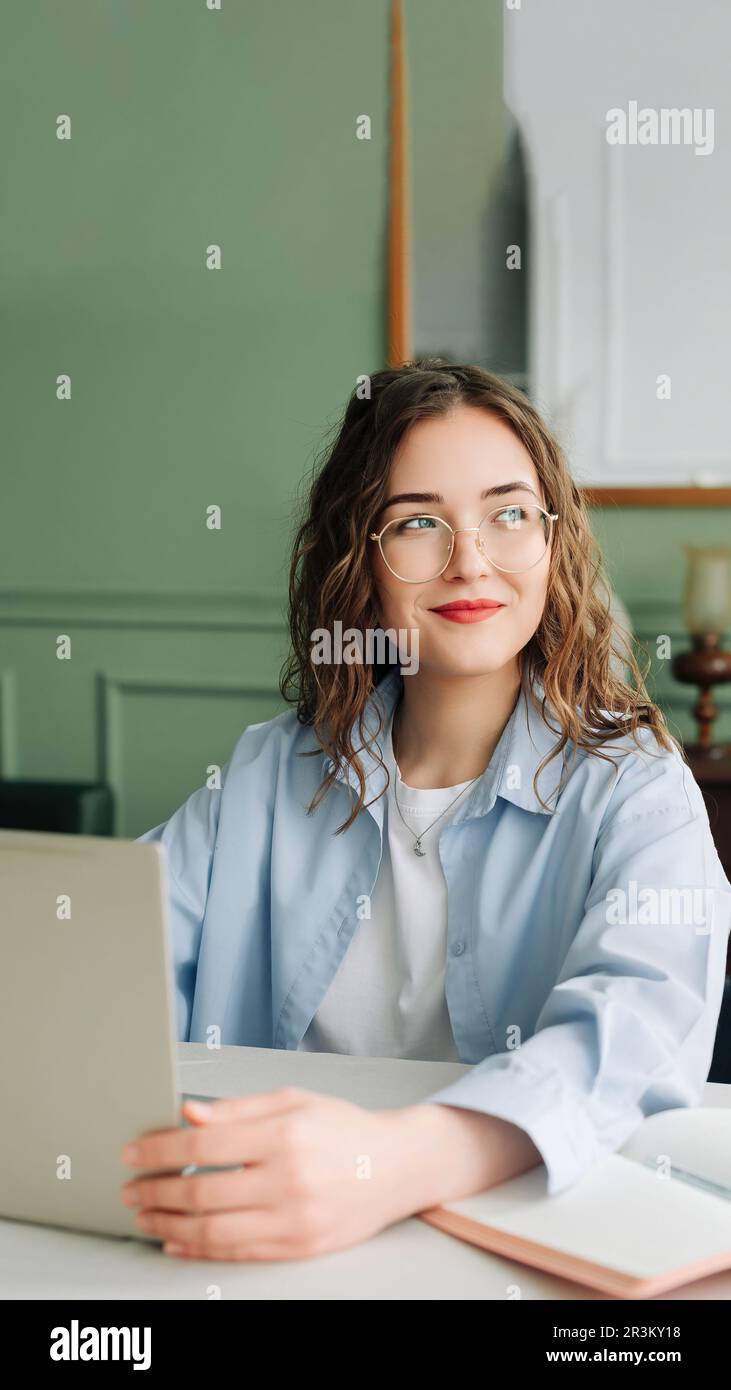 Lächelnde weibliche Mitarbeiterin, die in einem modernen Büro mit einem Notebook arbeitet, Marketingmanagerin oder Geschäftsfrau, die sich auf den Bildschirm konzentrierte, glücklich und selbstbewusst Stockfoto