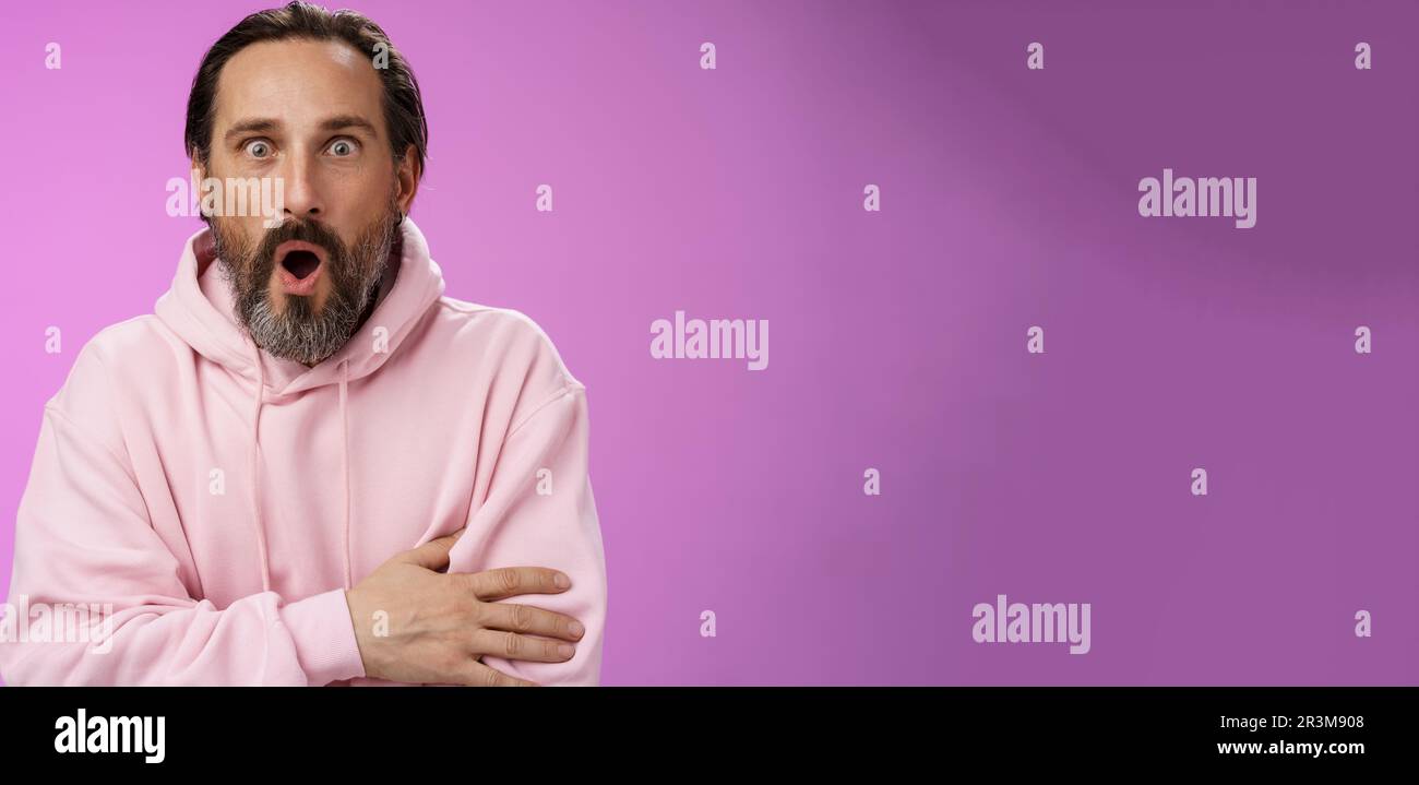 Schockiert beeindruckt Klatsch kaukasischen bärtigen Erwachsenen 40er Mann graue Haare in rosa Hoodie keuchend fasziniert Falten Lippen wow erweitern Augen Stockfoto