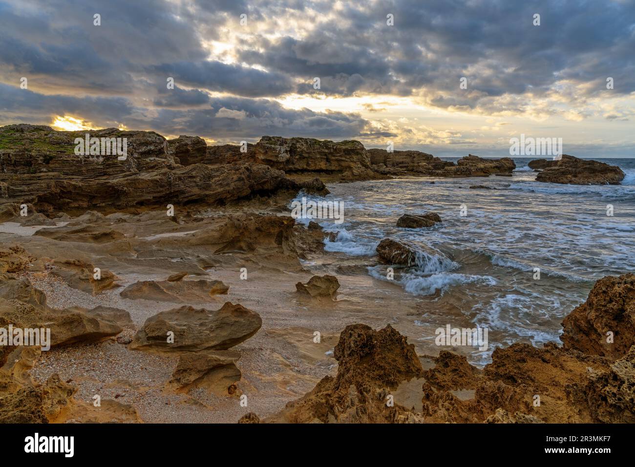 Eine felsige Bucht und ein Sandstrand unter einem ausdrucksstarken Sonnenuntergangshimmel an der zerklüfteten Westküste Sardiniens Stockfoto