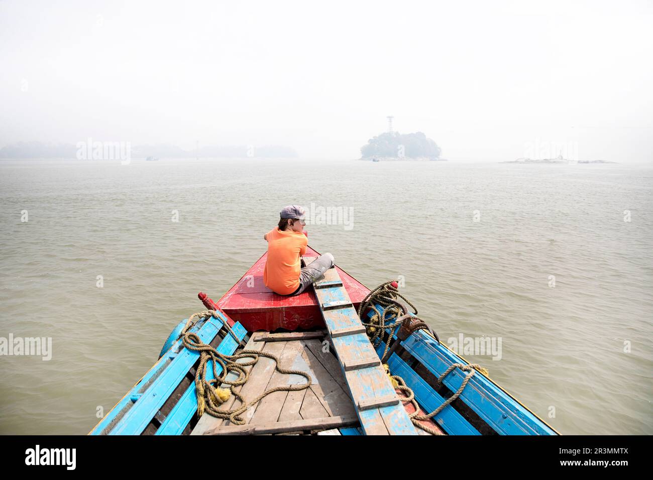 Touristenjunge auf einem traditionellen hölzernen Passagierboot auf dem Brahmaputra Fluss in der Nähe von Guwahati mit der Flussinsel hinten an einem nebeligen Sommertag, Assam, Indien Stockfoto