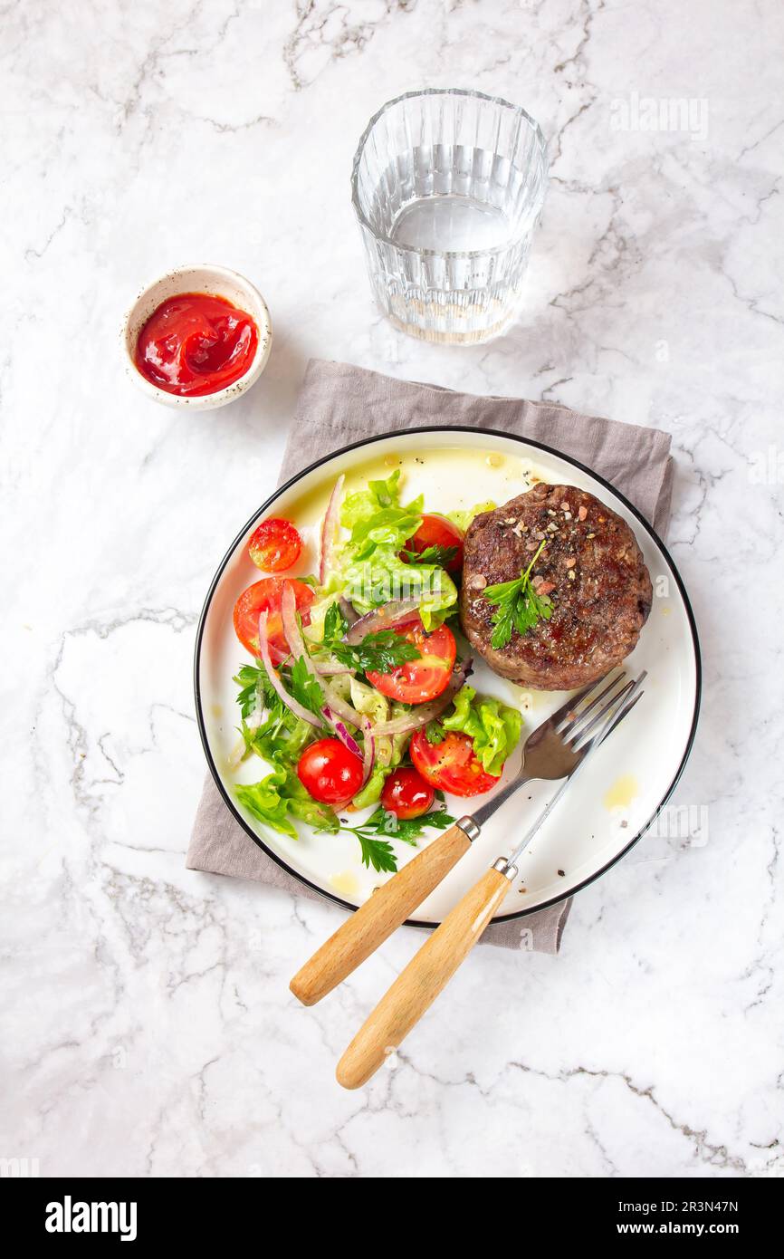 Rindfleisch-Hamburger mit Salat, Tomatensalat auf weißem Teller, Draufsicht Stockfoto