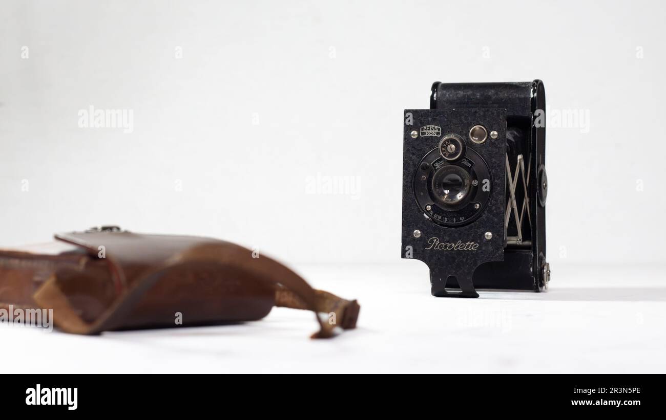 Eine alte Zeiss Ikon Piccolette Kamera aus dem 1920er neben einer klassischen Kodak Ledertasche auf reinem weißem Hintergrund Stockfoto