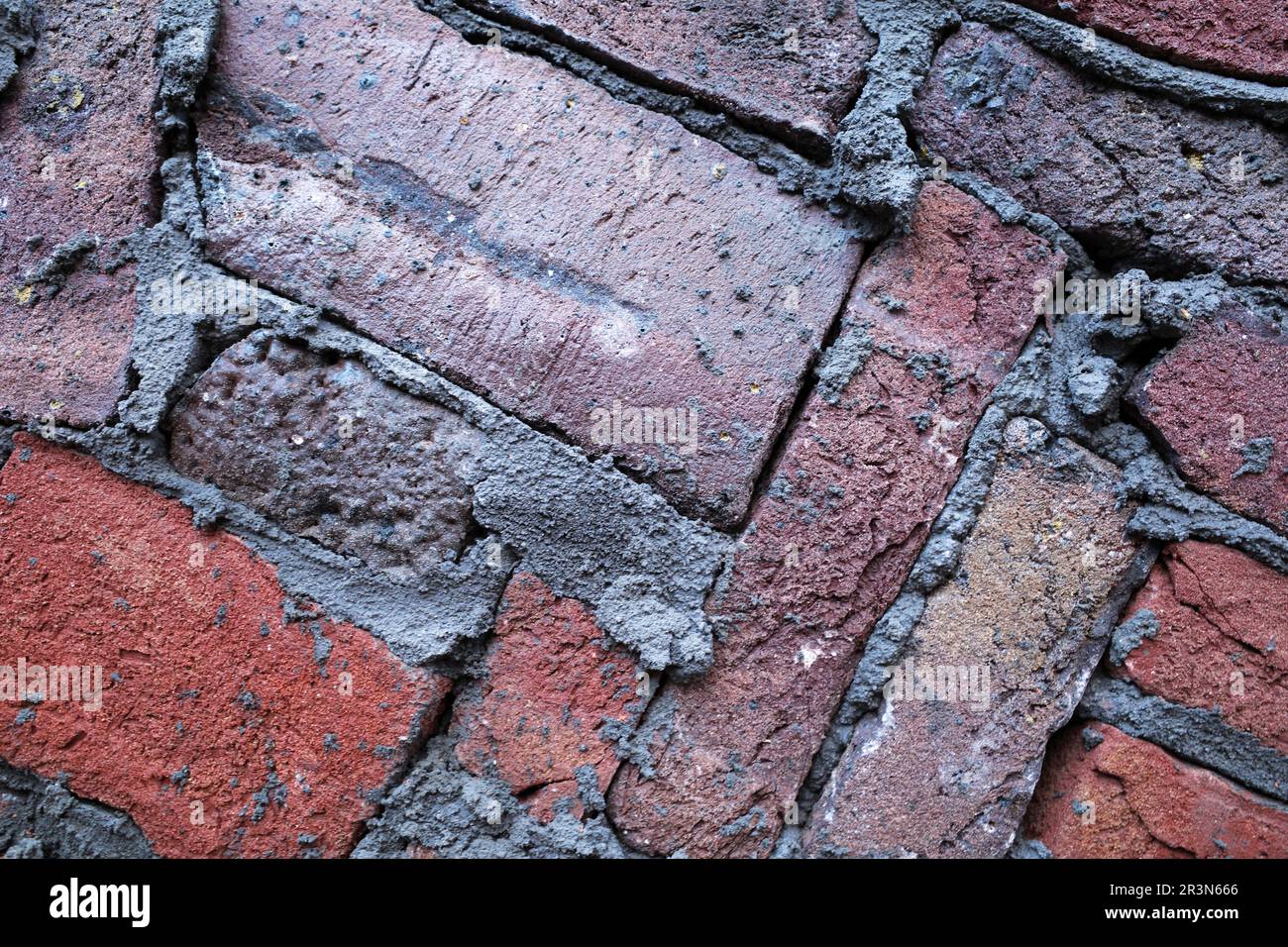 Eine moderne Mauer. Dunkelrote Ziegel sind kunstvoll verlegt und mit dunkelgrauem Zement verfugt. Stockfoto
