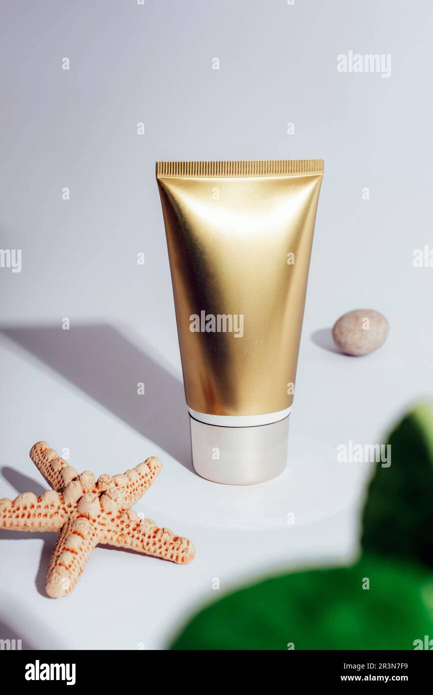 Goldene cremefarbene Röhre und Seesterne auf weißem Hintergrund mit harten Schatten. Sonnencreme, Naturkosmetik-Konzept. Nahaufnahme. Stockfoto