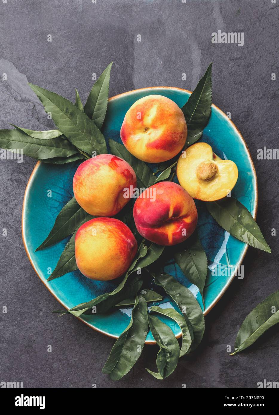 Frischer reifer Pfirsich mit Pfirsichblättern auf blauem Teller, Draufsicht Stockfoto