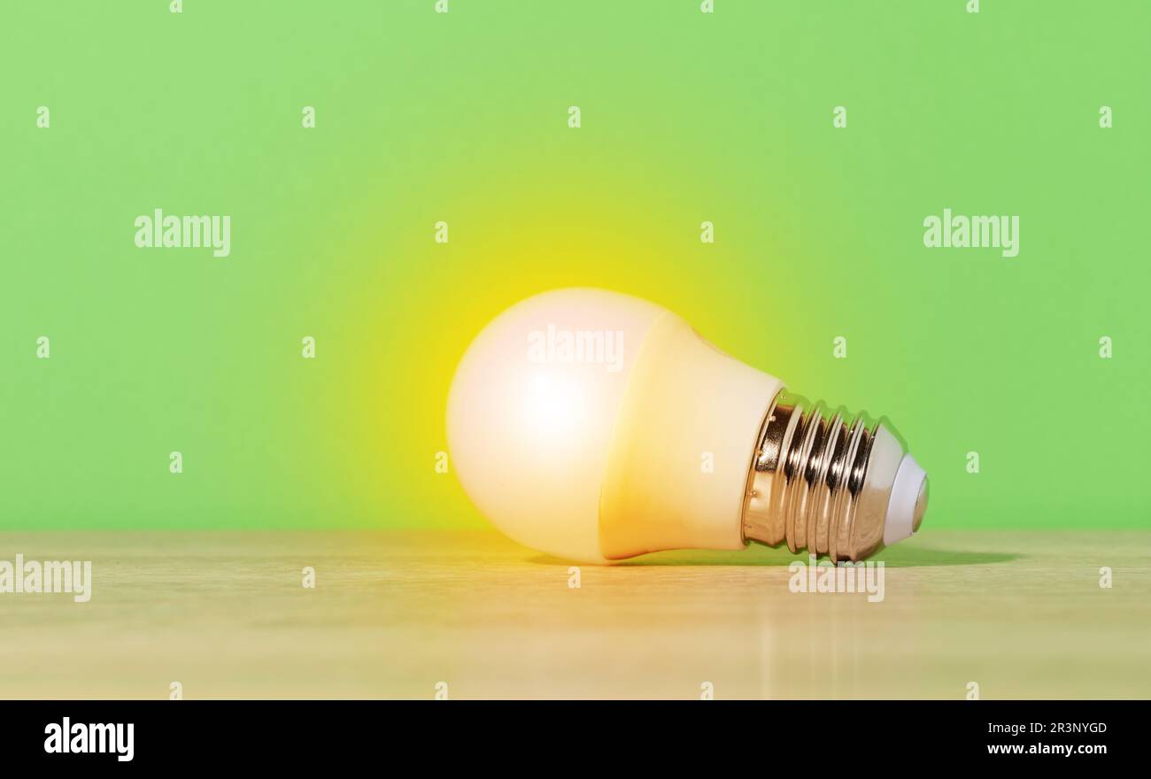 Eine glasweiße Lampe leuchtet mit gelbem Licht auf grünem Hintergrund. Neue Idee Stockfoto