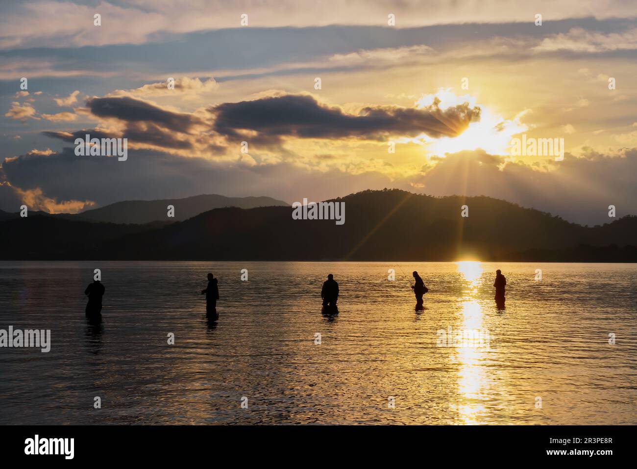 Silhouetten von Fischern vor dem Hintergrund der untergehenden Sonne, Wolken und Silhouetten von Bergen, selektiver Fokus, Idee für einen Hintergrund oder eine Wal Stockfoto