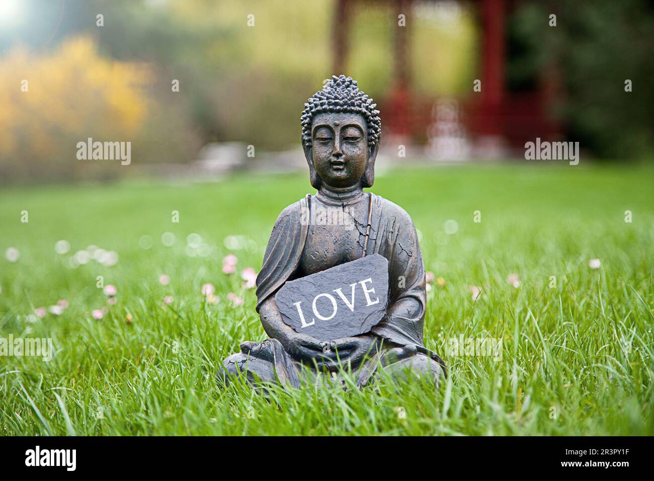 Buddha-Statue auf einer Wiese mit einem Schild mit der Aufschrift "Love" Stockfoto