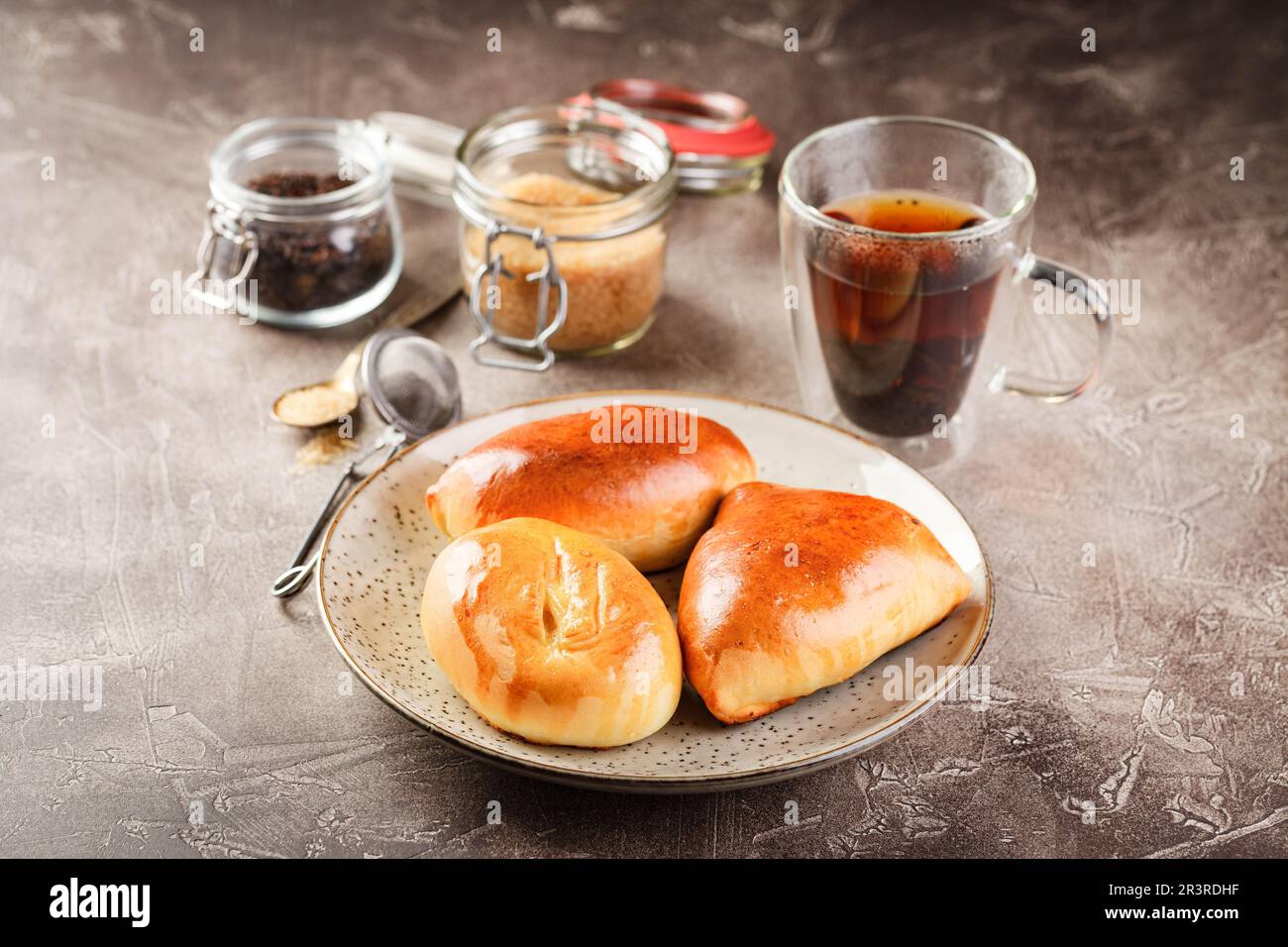 Süße Hefeteigkuchen mit verschiedenen Füllungen auf Platte und Glas Tee Stockfoto