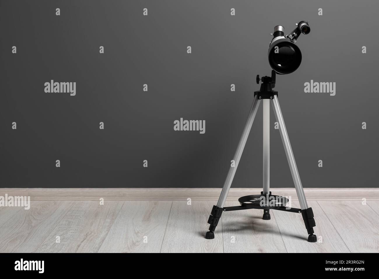 Stativ mit modernem Teleskop nahe der grauen Wand. Platz für Text Stockfoto