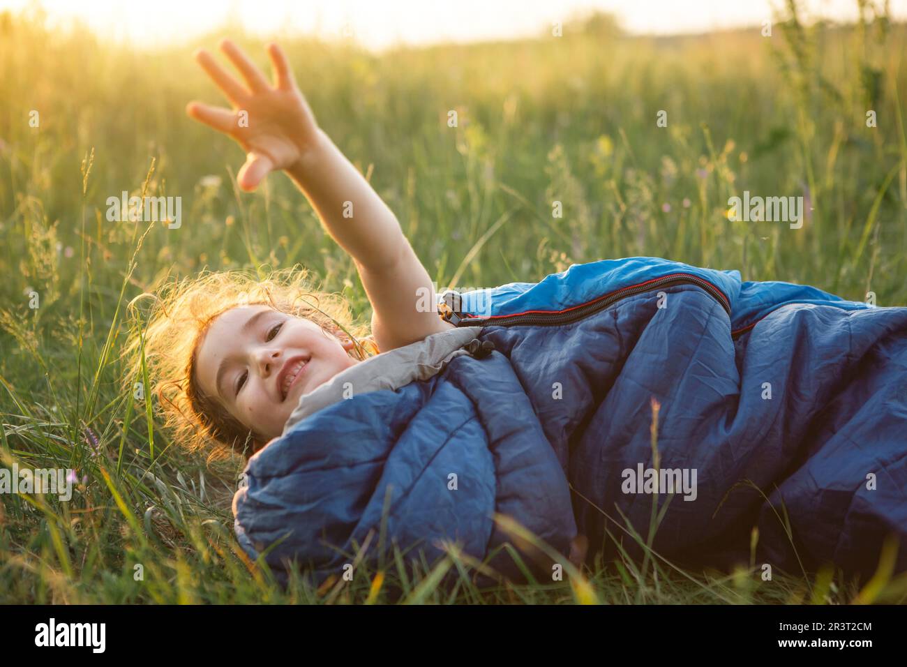 Ein Kind schläft in einem Schlafsack auf dem Rasen bei einem Campingausflug - umweltfreundliche Erholung im Freien, gesunder Lebensstil, Summer tim Stockfoto