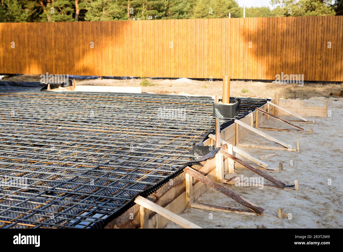 Eisenbeschläge auf einer Holzschalung mit verlegten Rohren bilden die Grundlage für das Gießen des Fundaments des Hauses mit einer Betonplatte. C Stockfoto