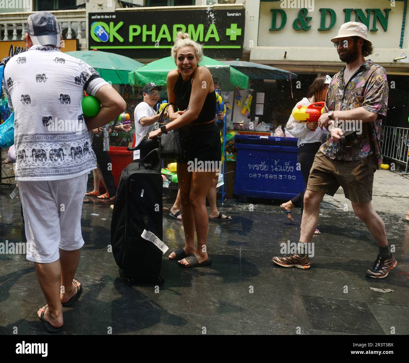 Falsche Zeit, falscher Ort. Eine Tourist, die mit ihrem Koffer auf der Khaosan Road spaziert und während des Songkran Festivals mit Wasser überschwemmt wird. Bangkok, Thailand. Stockfoto