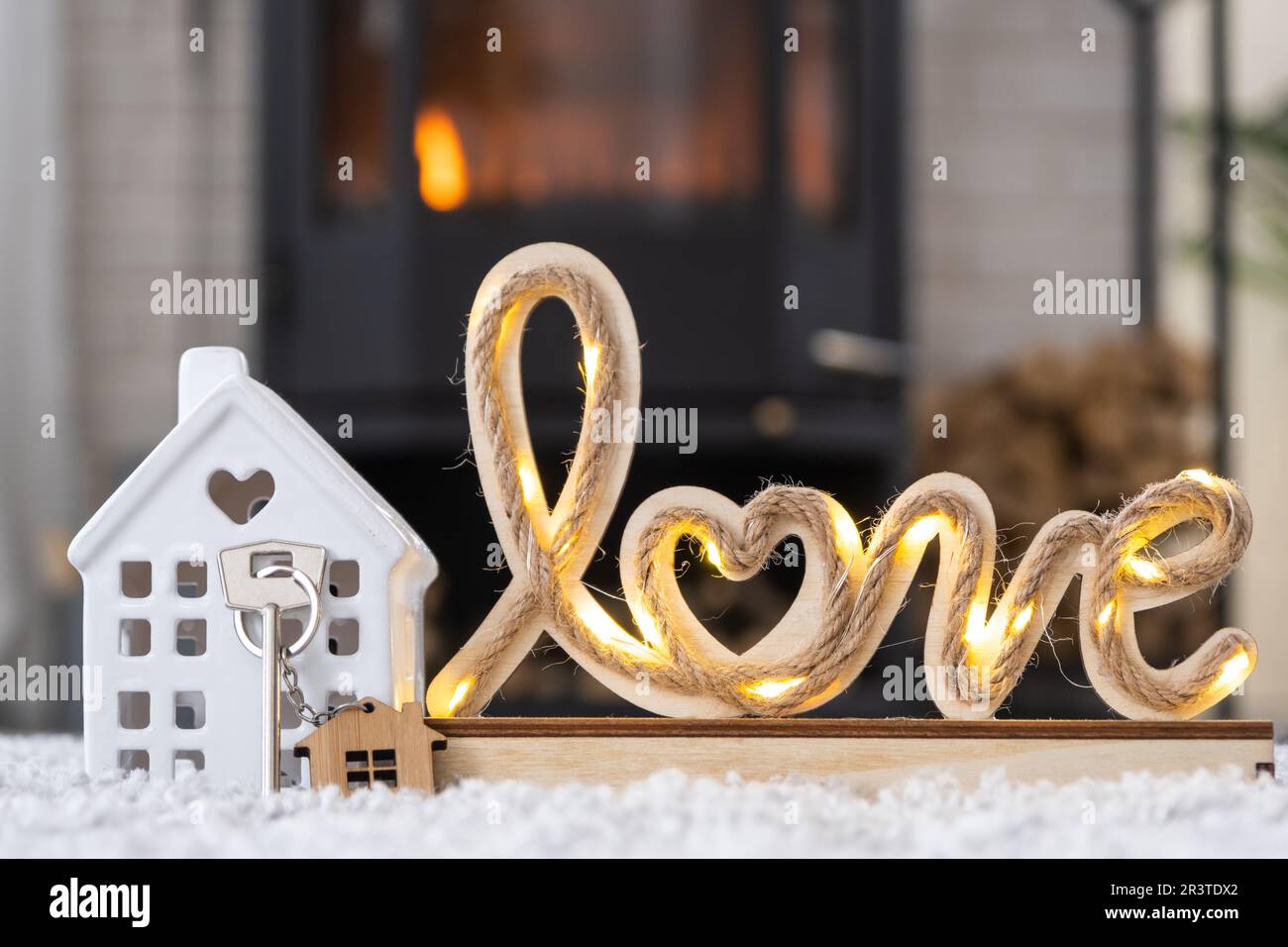 Schlüssel zum Haus mit Schlüsselanhänger vor dem Hintergrund von Kamin mit Kamin und Kaminholz im Valentinstag-Dekor, Liebes Zuhause. Ich ziehe nach Stockfoto