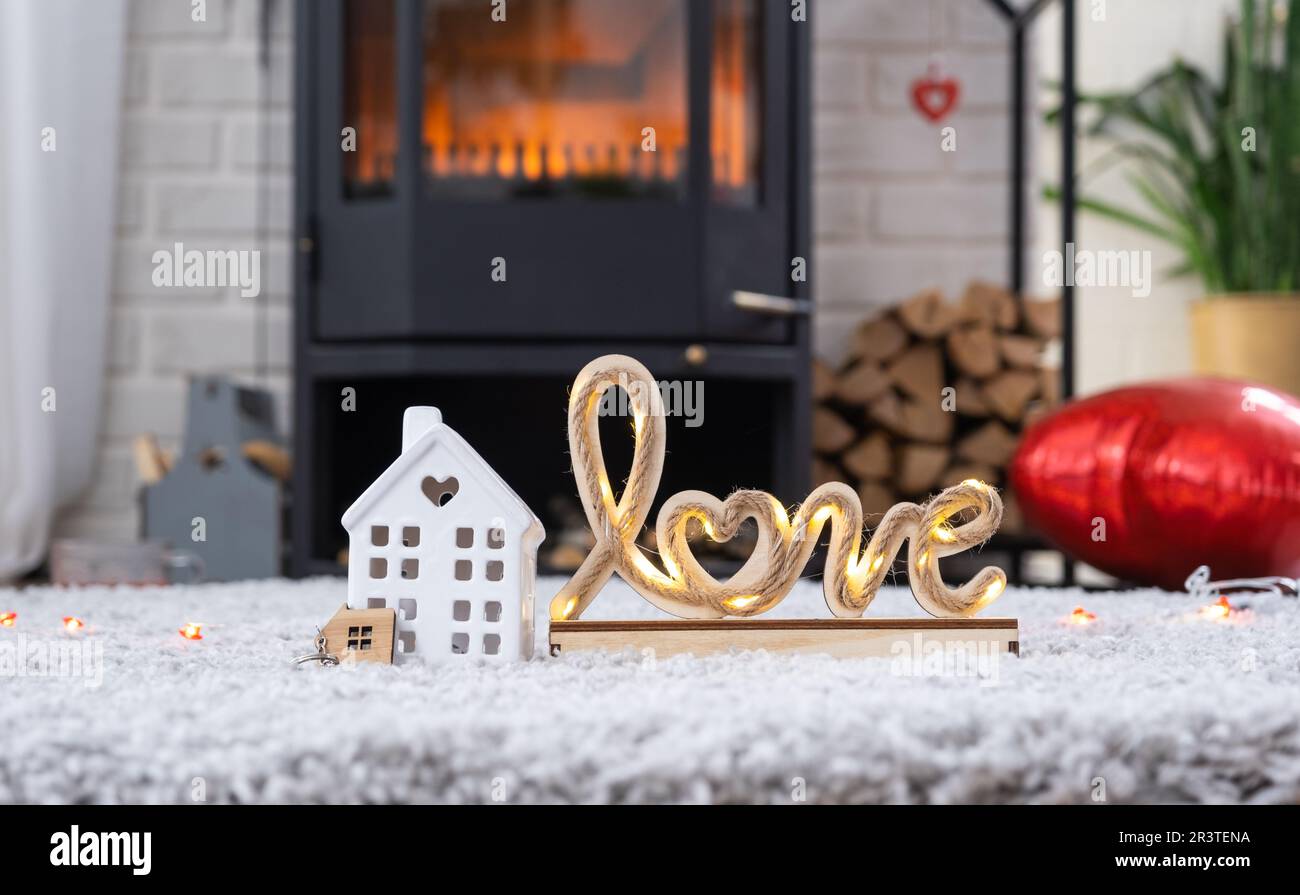 Schlüssel zum Haus mit Schlüsselanhänger vor dem Hintergrund von Kamin mit Kamin und Kaminholz im Valentinstag-Dekor, Liebes Zuhause. Ich ziehe nach Stockfoto