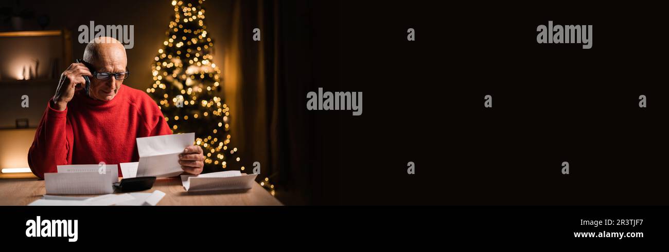 Wütende alte Männer mit Brille, die telefonieren und Rechnungen halten während der weihnachtsfeier, spät nachts arbeiten, überarbeitet, allein, reife Leute Stockfoto