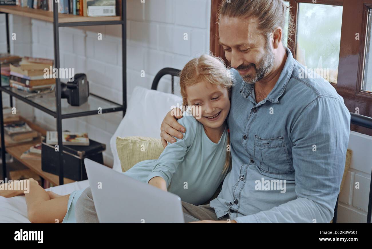 Vater benutzt Laptop-Computer mit der kleinen Tochter. Glückliche Familie, Vater entspannt sich und genießt es, zu Hause online zu arbeiten, während das kleine süße Mädchen im Bett liegt Stockfoto