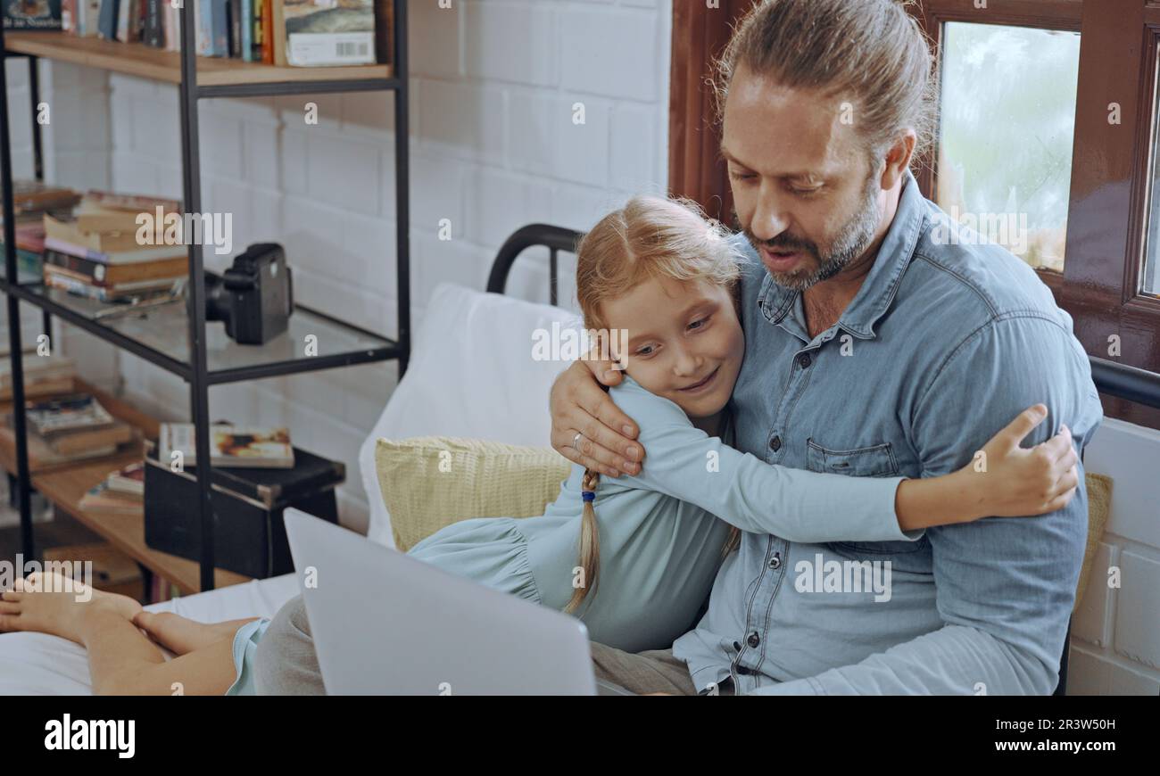 Vater benutzt Laptop-Computer mit der kleinen Tochter. Glückliche Familie, Vater entspannt sich und genießt es, zu Hause online zu arbeiten, während das kleine süße Mädchen im Bett liegt Stockfoto