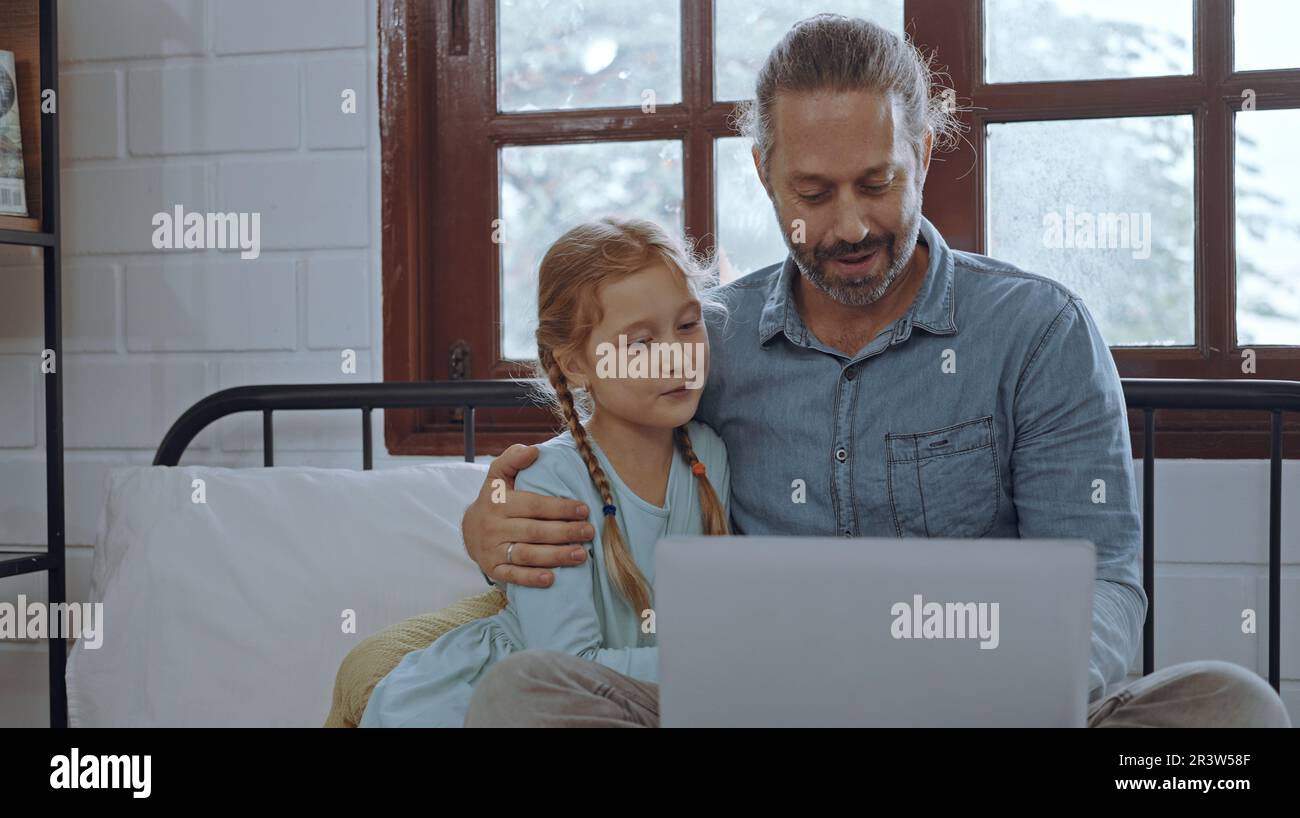Vater benutzt Laptop-Computer mit der kleinen Tochter. Glückliche Familie, Vater entspannt sich und genießt es, zu Hause online zu arbeiten, während das kleine süße Mädchen im Bett liegt Stockfoto
