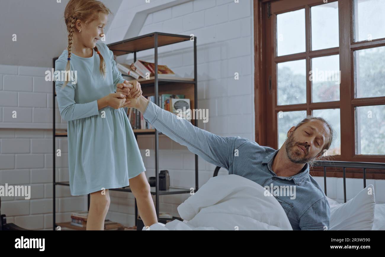 Die Tochter wacht den Vater morgens im Bett auf. Stockfoto