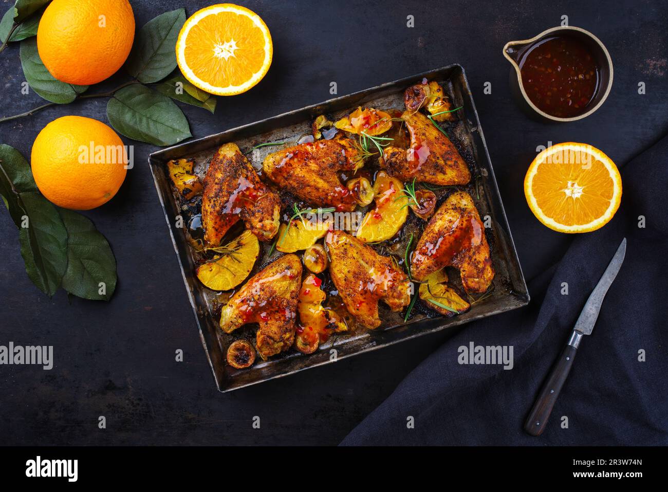 Traditionelle Barbecue-Hähnchenflügel mit Orangen- und Bananenscheiben, serviert mit heißer Chilisauce als Draufsicht auf einem rustikalen Metalltablett Stockfoto