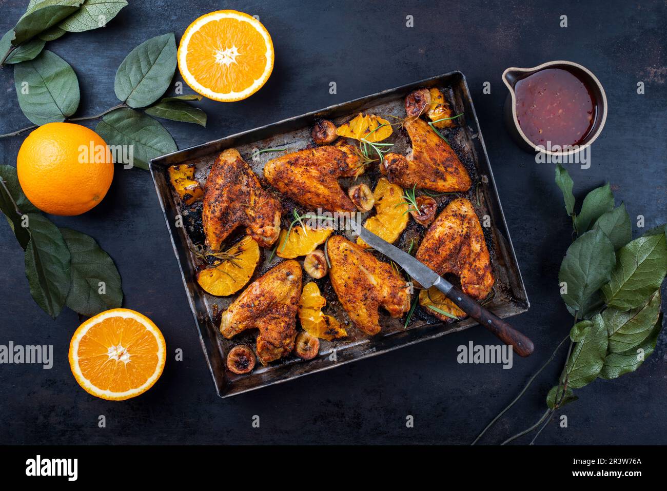 Traditionelle Barbecue-Hähnchenflügel mit Orangen- und Bananenscheiben, serviert mit heißer Chilisauce als Draufsicht auf einem rustikalen Metalltablett Stockfoto