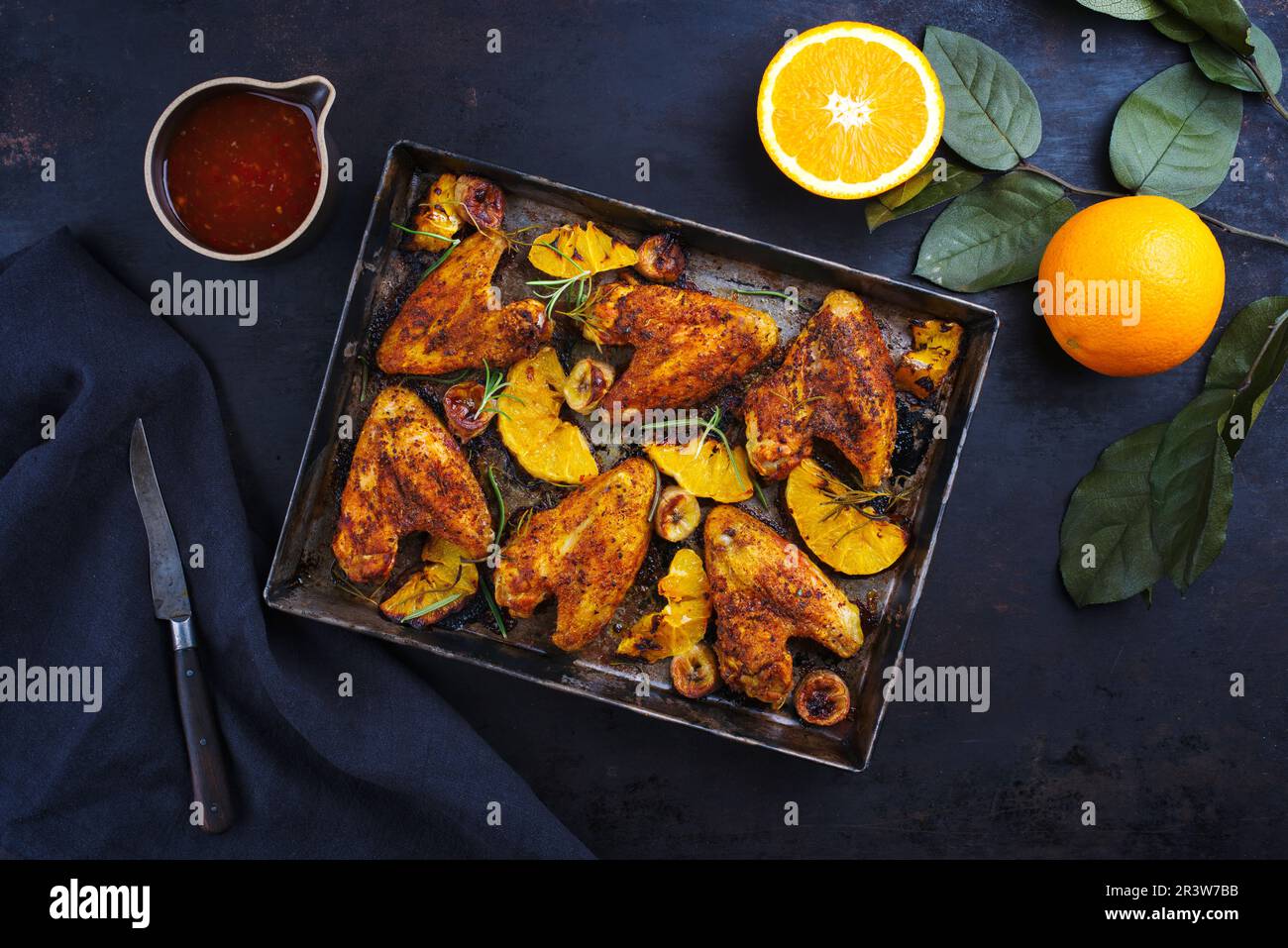 Traditionelle Barbecue-Hähnchenflügel mit Orangen- und Bananenscheiben, serviert mit heißer Chilisauce als Draufsicht auf einem rustikalen Metalltablett Stockfoto