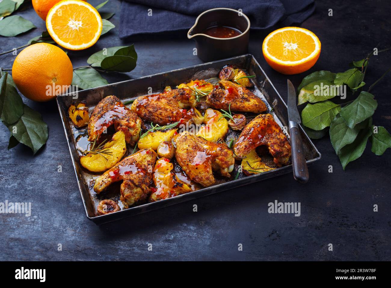 Traditionelle Barbecue-Hähnchenflügel mit Orangen- und Bananenscheiben, serviert mit heißer Chilisauce aus der Nähe auf einem rustikalen Metalltablett Stockfoto