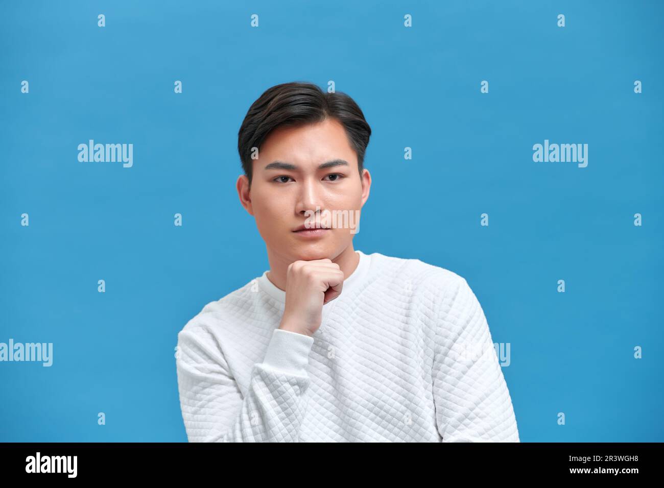 Ein durchdachter, komplizierter asiatischer Mann im Hemd, berührt das Kinn auf blauem Hintergrund Stockfoto