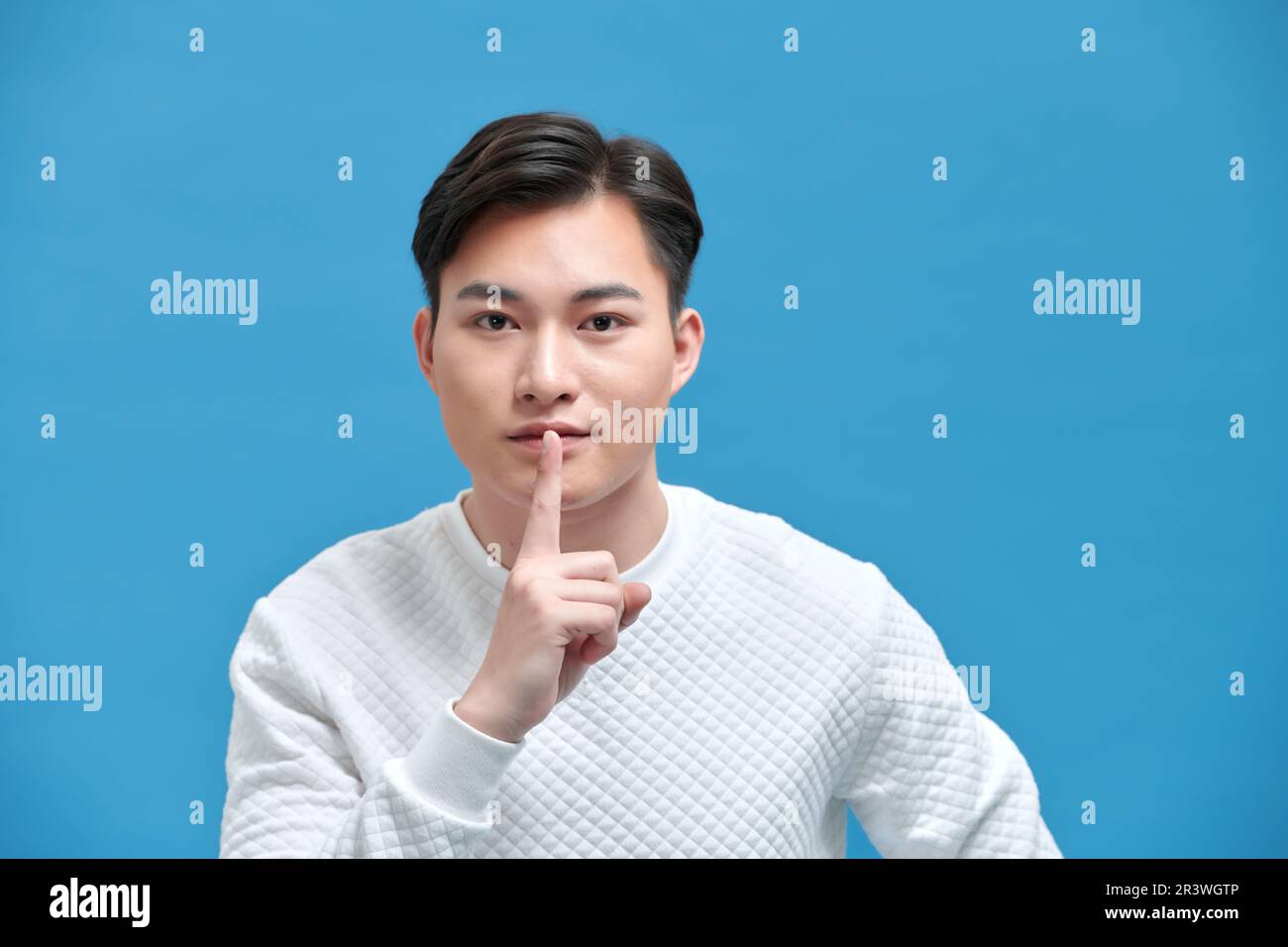 Porträt eines seriösen jungen Asiaten, der ein Zeichen der Stille zeigt, indem er die Finger in den Mund steckt Stockfoto